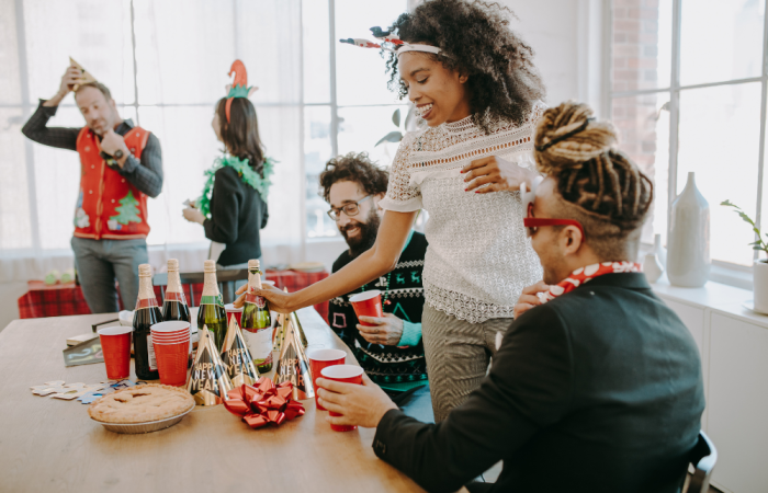 A group of people wearing holiday attire enjoy festive drinks together in a brightly lit room.